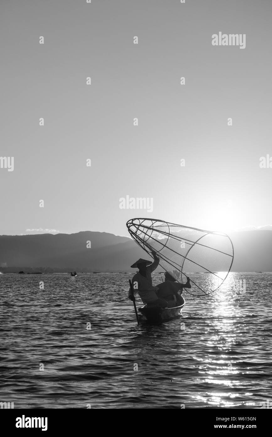 Immagine in bianco e nero del pescatore locale silhouette tenendo una tradizionale rete a Lago Inle durante il tramonto, Myanmar Foto Stock