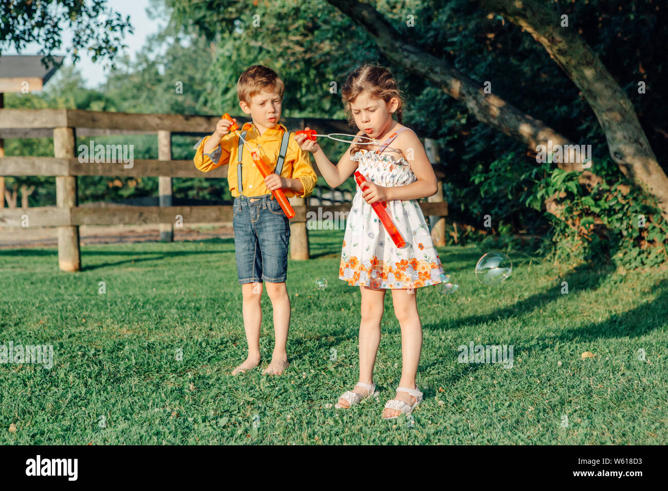 Ritratti di divertente piccola bionda caucasica ragazza bambino soffia bolle di sapone nel parco al tramonto d'estate. Vero e autentico infanzia felice momento. La vita Foto Stock