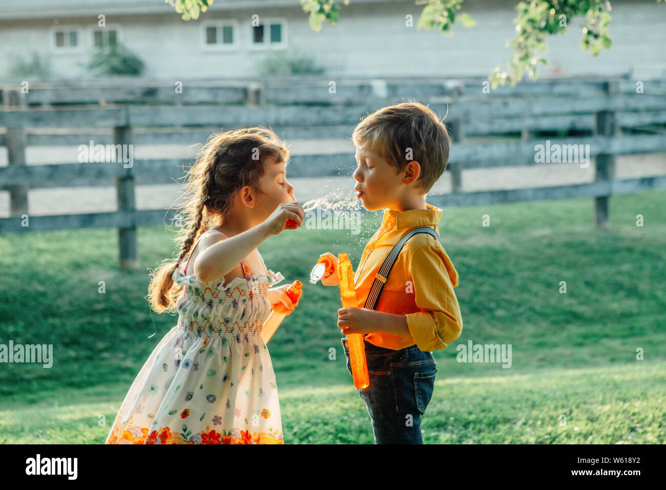 Divertenti bambini caucasici ragazzo e una ragazza soffia bolle di sapone nel parco al tramonto d'estate. Vero e autentico infanzia felice momento di amicizia. Stile di vita ac Foto Stock