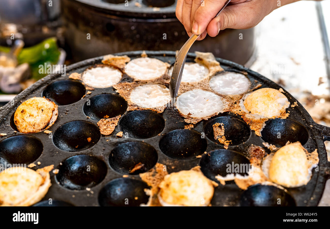 Malta-pasticceria tostato o 'Kanom Krok' è Thai dessert tradizionale. Donna mano rimozione Kanom Krok da stufa dal cucchiaio. Cucina di strada in Thailandia. Thai Foto Stock