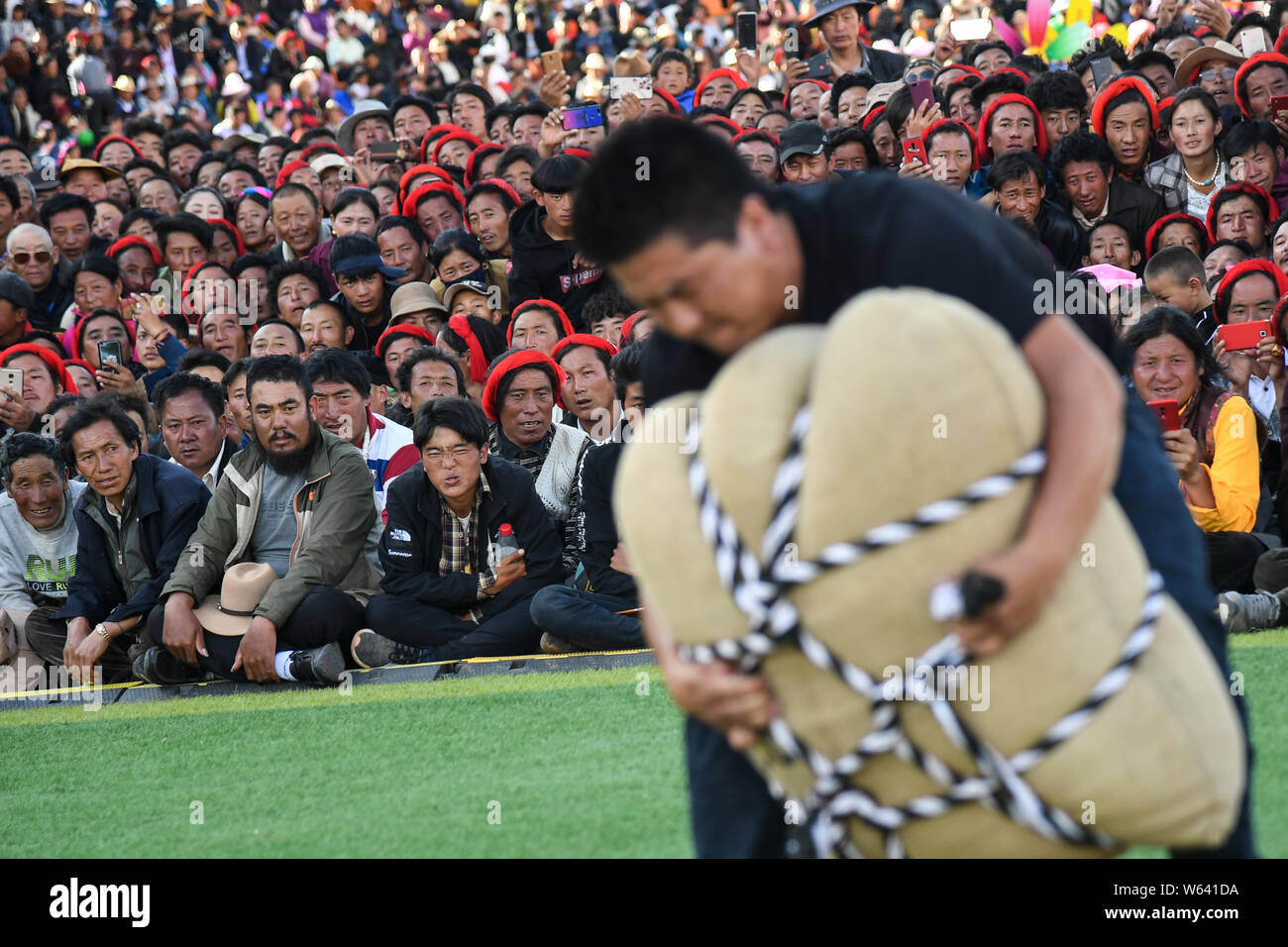 Tibetana locale le persone reagiscono come si guarda a un partecipante di sollevamento di un contrappeso durante un uomo forte sfida nella contea di Markam, Chamdo città, a sud-ovest della Cina" Foto Stock