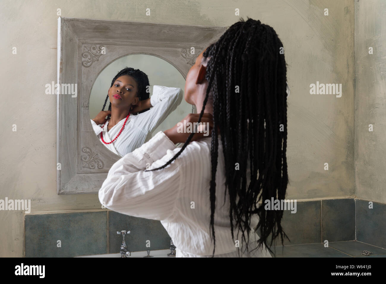 Piuttosto giovane americano africano donna facendo la sua routine mattutina nella parte anteriore dello specchio del bagno Foto Stock