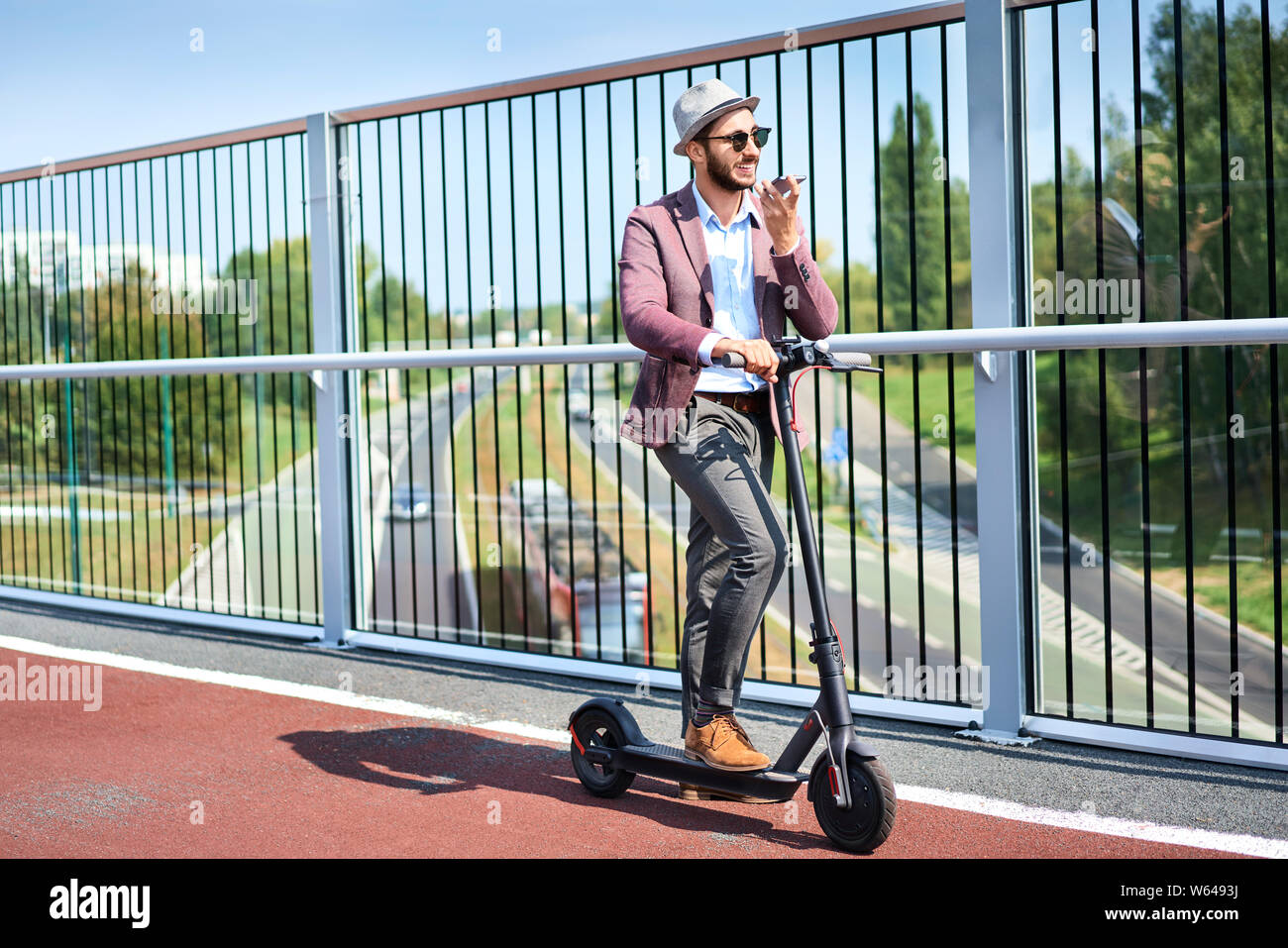 Giovane uomo in piedi su scooter motorizzato nella città e parlando al telefono Foto Stock