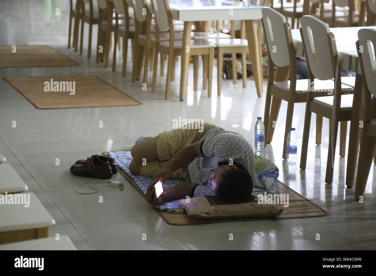 Un genitore di uno studente matricole, che ha accompagnato il suo bambino per la registrazione sul suo primo giorno di studio, dorme sul pavimento in corrispondenza di una mensa in una università in Z Foto Stock
