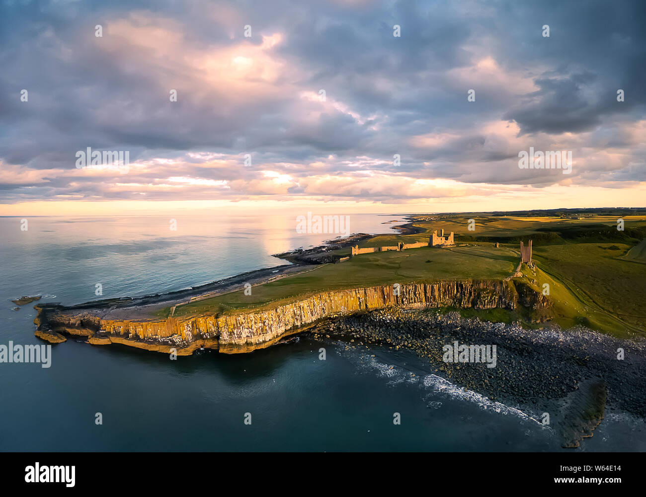 Vista dall'aereo alla Embleton riva del mare, mare del Nord, la rupe con i gabbiani, le rovine e i verdi campi. Tramonto con nuvole drammatico. Paese Inghilterra Foto Stock