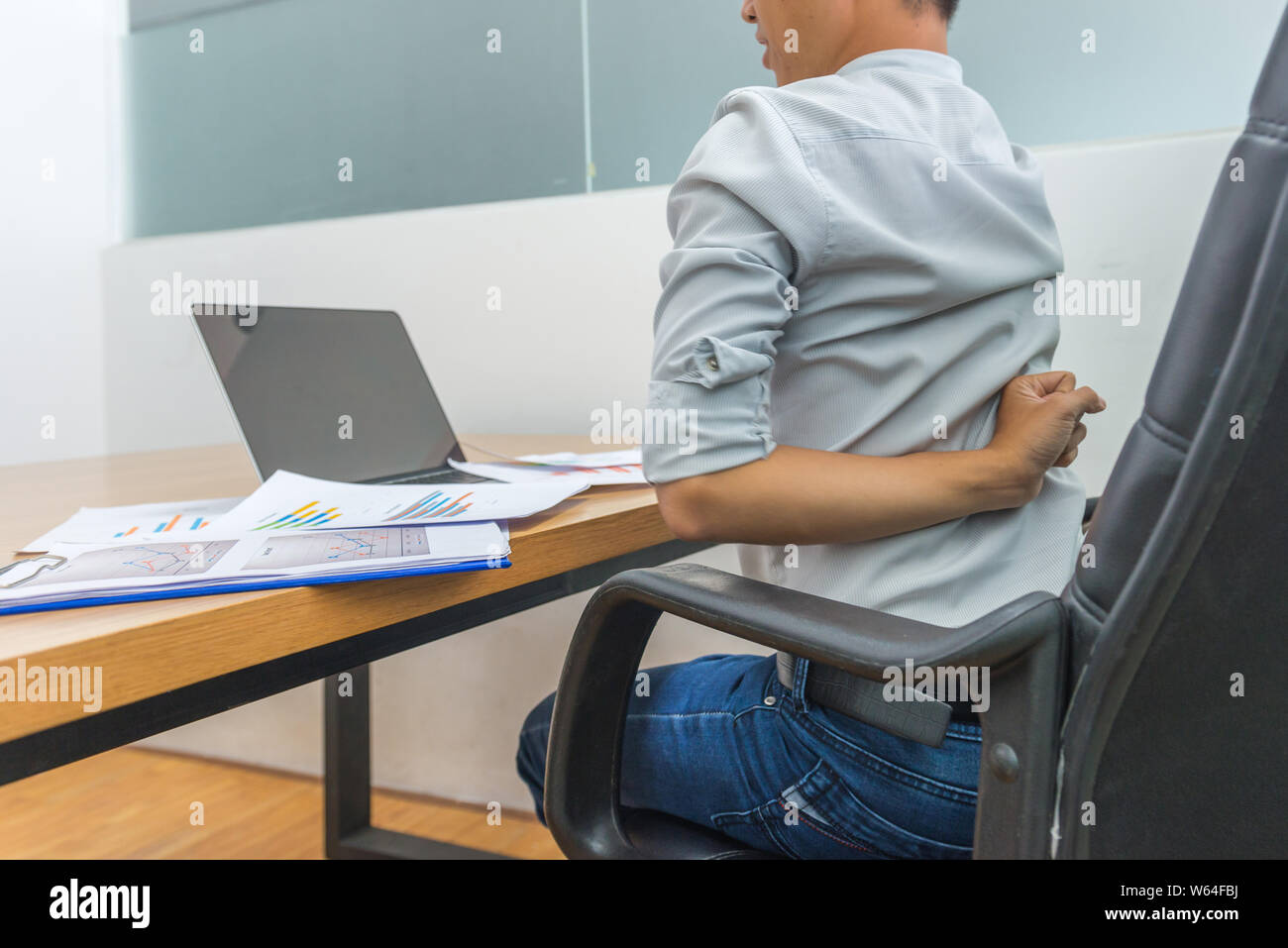 Lavoratore di ufficio avente il dolore alla schiena seduta nella parte anteriore del computer portatile Foto Stock
