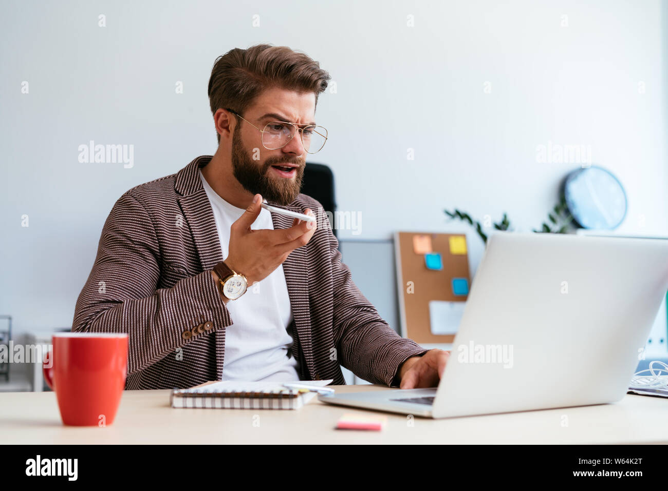 Avvio concentrato imprenditore parlando al telefono con la modalità altoparlante mentre guarda il computer portatile in ufficio Foto Stock