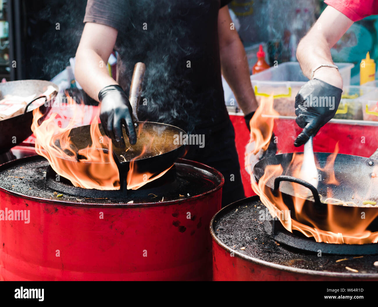 La cottura di cibi in vaschette a un festival di strada, il fuoco con il rosso di barili. Foto Stock