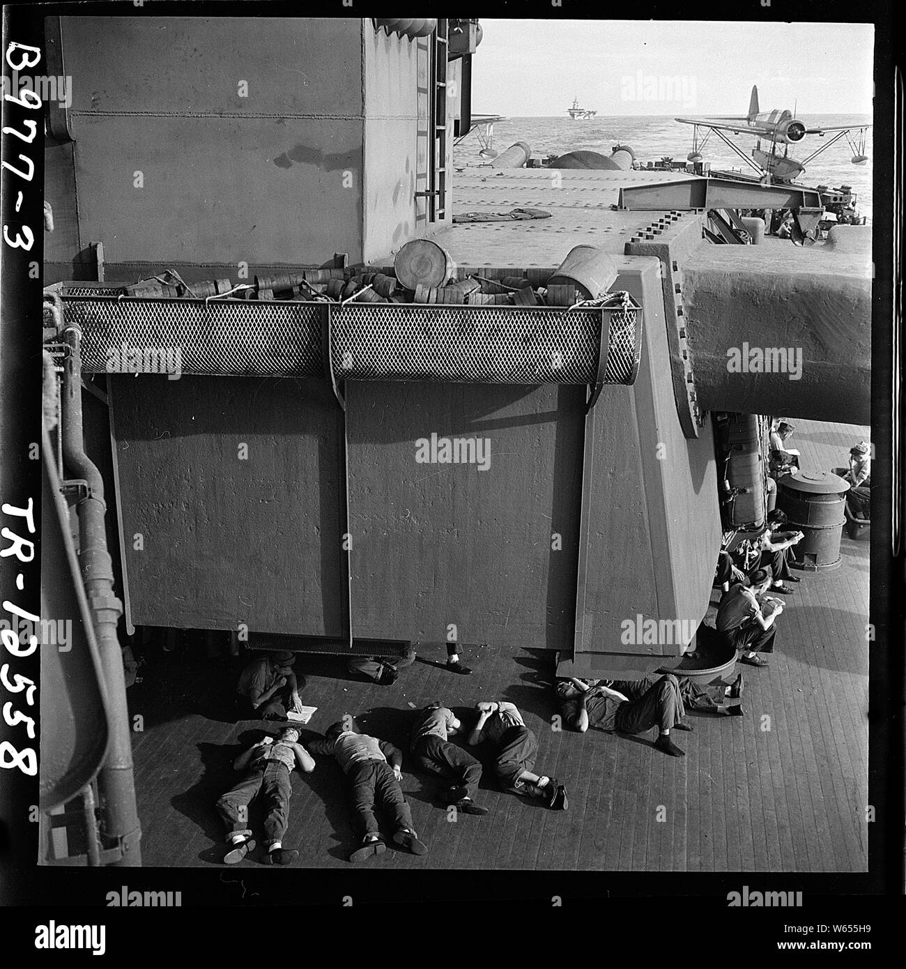 Uomini arruolati rilassante durante off-dovere ore a bordo della USS New Jersey (BB-62) OS2U su di una catapulta in background. Foto Stock