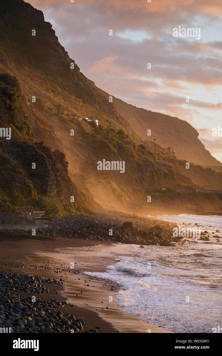 Tramonto a spiaggia accanto al green mountain range in controluce Foto Stock