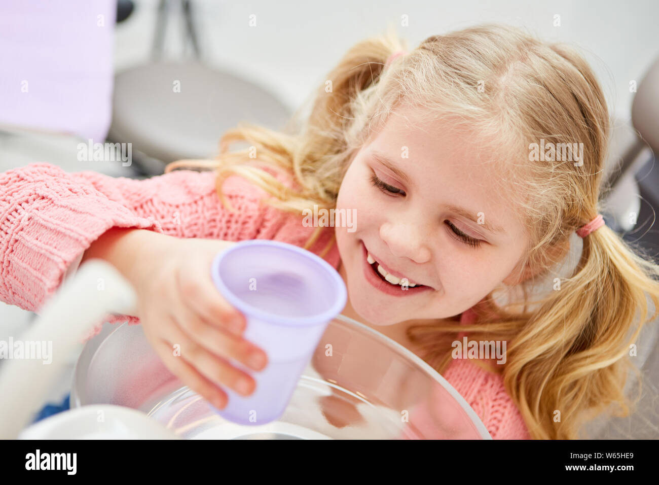 La ragazza alla dentista sciacqua la bocca con un bicchiere d'acqua durante il trattamento Foto Stock
