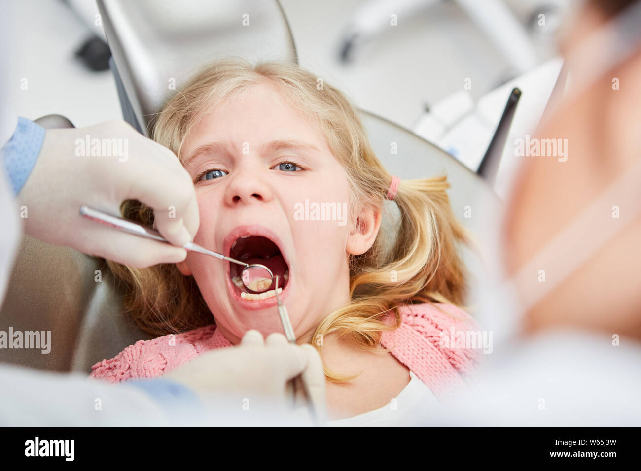Dentista con specchio esamina i denti di poco in ansia ragazza alla prospettiva di carie Foto Stock