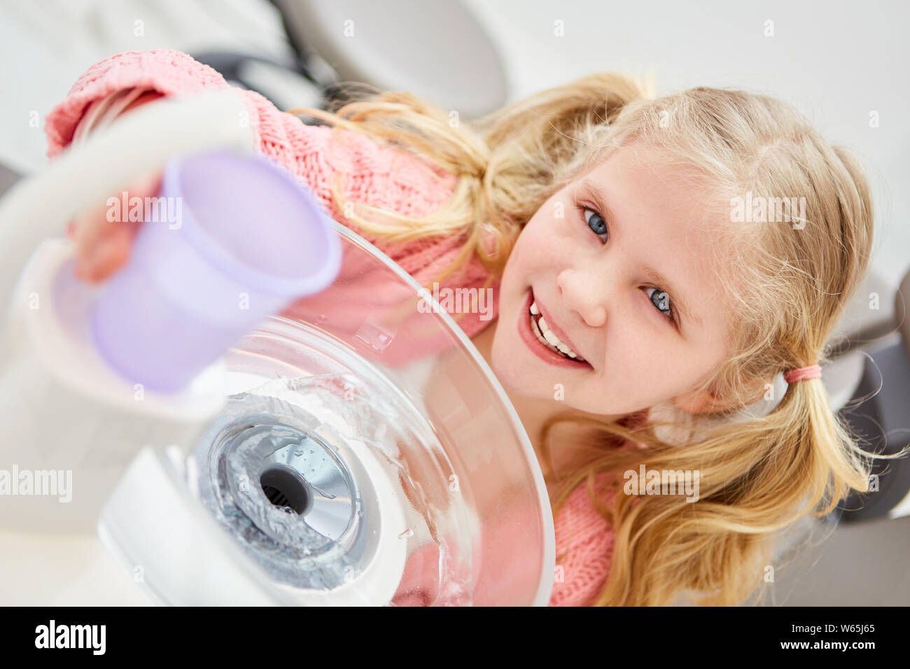 Bambino felice dal dentista con una tazza di plastica di acqua per il risciacquo per igiene dentale Foto Stock