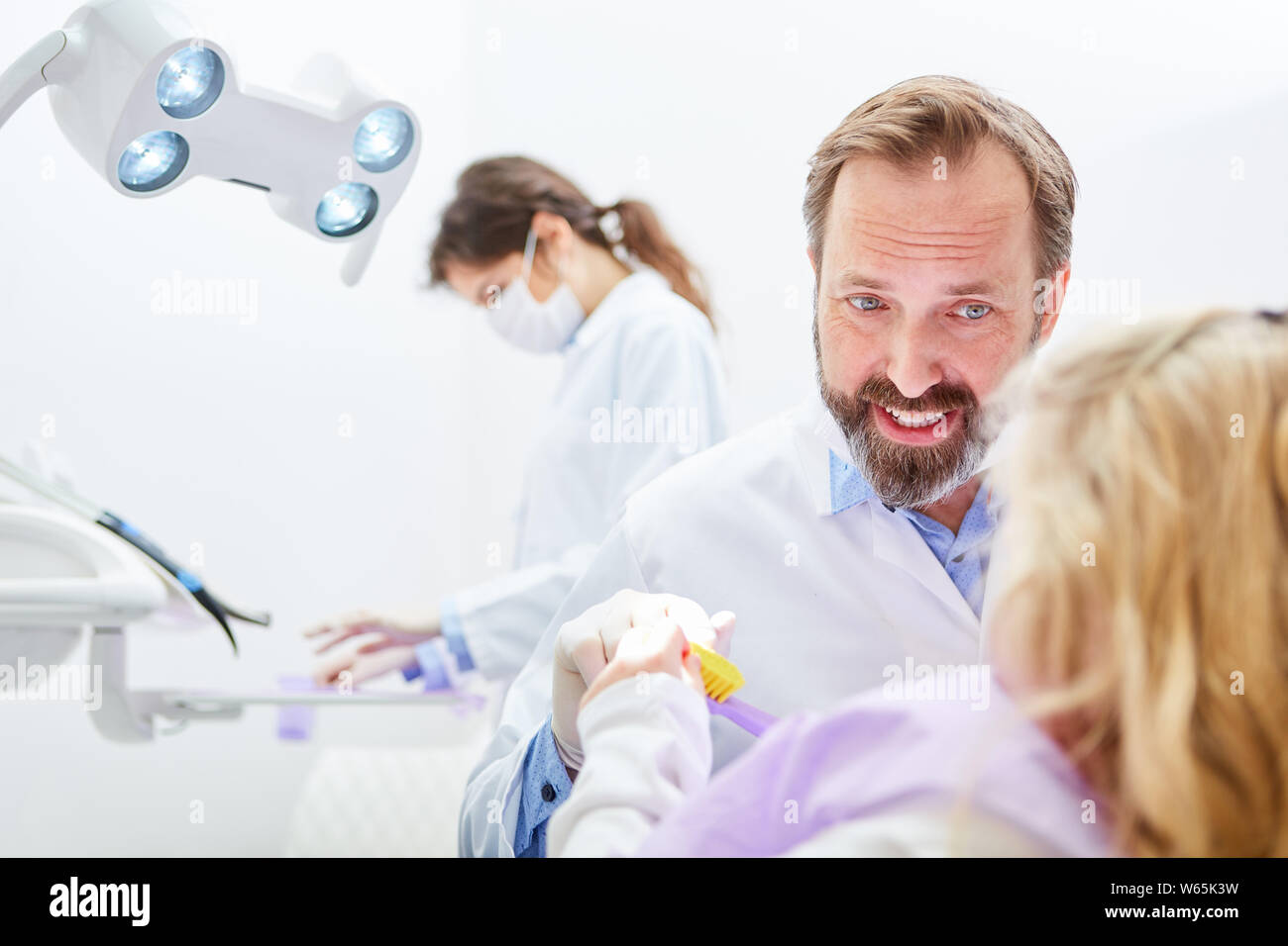 Dentista spiega bambino corretta spazzolatura dei denti per la salute dentale con uno spazzolino da denti Foto Stock