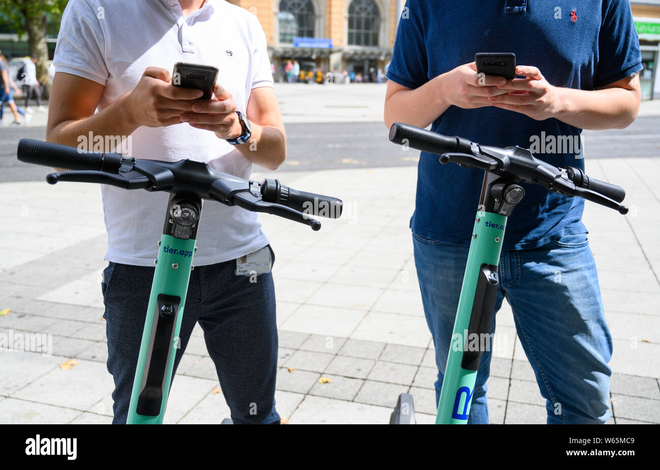 Hannover, Germania. 31 Luglio, 2019. Due uomini noleggiare un'app E-Tretroller del provider "Tier" sul Ernst-August Platz davanti la stazione principale. Per la prima volta uno scooter elettrico servizio di noleggio è lanciato in Hannover. Credito: Christophe Gateau/dpa/Alamy Live News Foto Stock