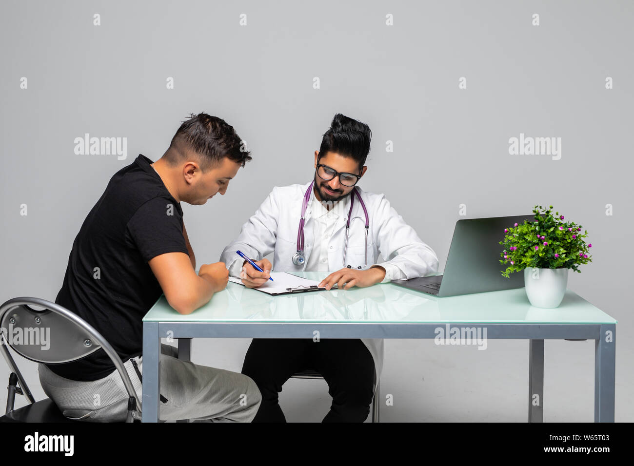Indian medico prescrive la prescrizione per pacient seduto alla scrivania ufficio medico, isolato su sfondo bianco Foto Stock