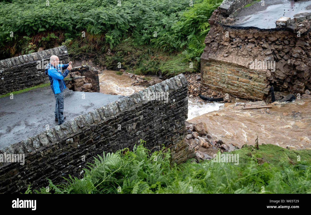 Un uomo prende una fotografia di un ponte crollato vicino Grinton, North Yorkshire, dopo le parti della regione avevano fino a 82.2mm di pioggia in 24 ore il martedì. Foto Stock