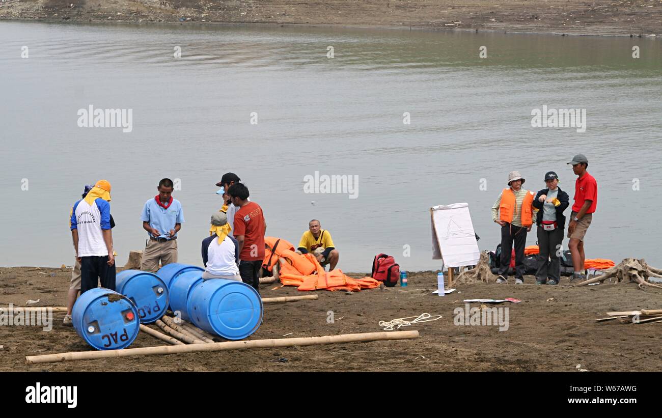 Un gruppo di giovani si riuniscono accanto ad una diga d'acqua e si prevede di fare una barca con barili di plastica blu, bastoni di bambù e corde. Foto Stock