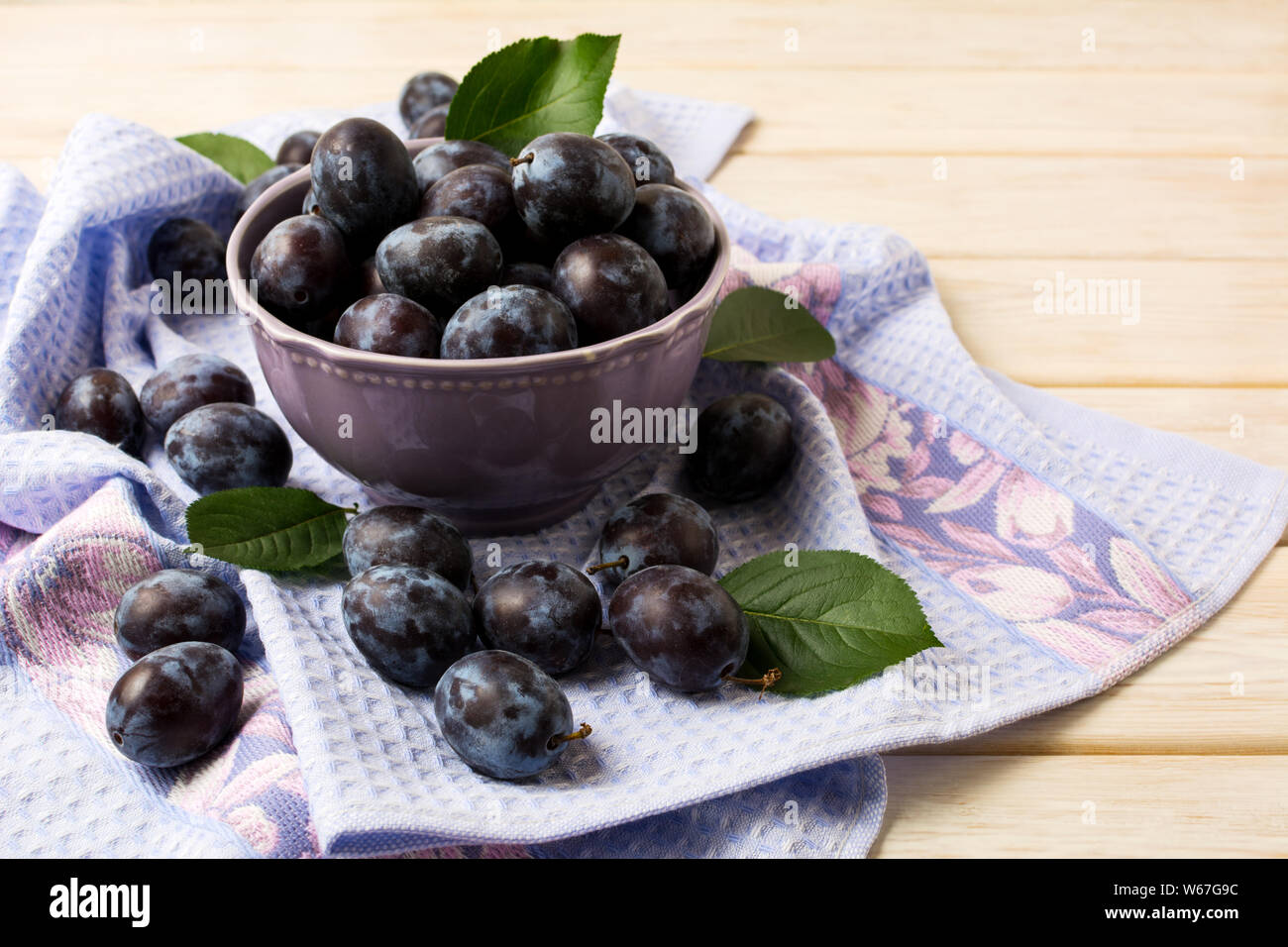 Vaso in ceramica con prugne fresche e blu tovagliolo rustico sul bianco tavolo in legno Foto Stock