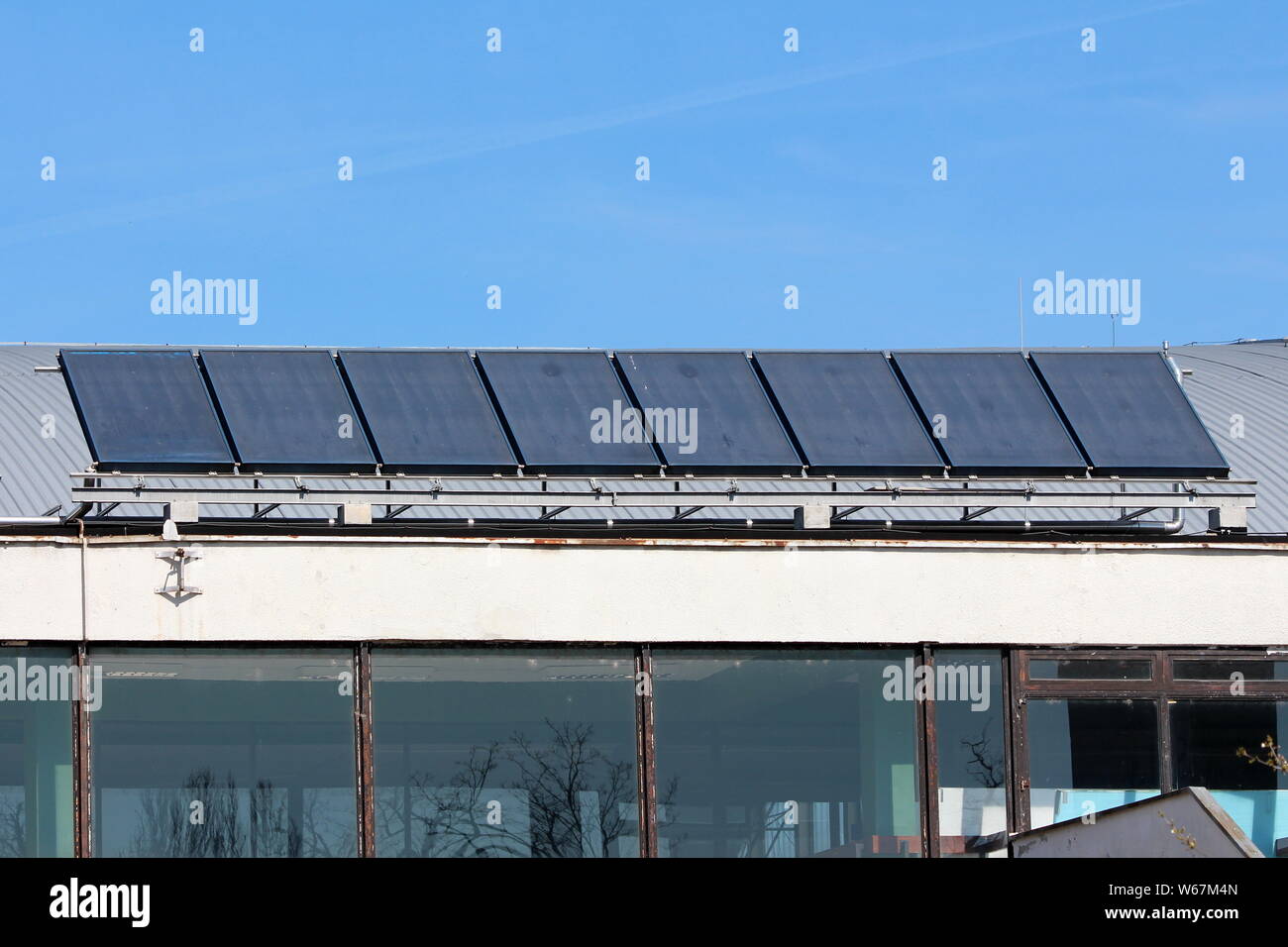 Fila di grande buio riscaldamento di acqua solare pannelli montati sulla parte superiore del vecchio tetto metallico del locale sala sportiva sulla calda soleggiata giornata di primavera Foto Stock