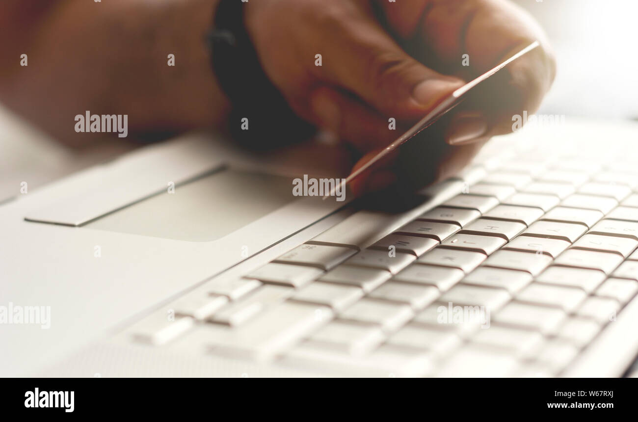Mano di sesso maschile in possesso di una carta di credito durante il pagamento via internet transazione. Concetto di e-commerce e shopping on line. Foto Stock