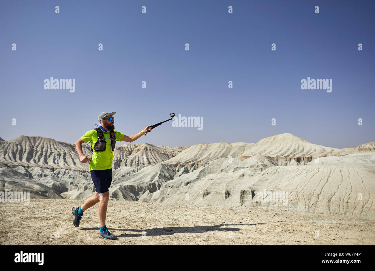 Runner atleta con la barba in esecuzione su montagne bianche nel deserto con la fotocamera di azione Foto Stock