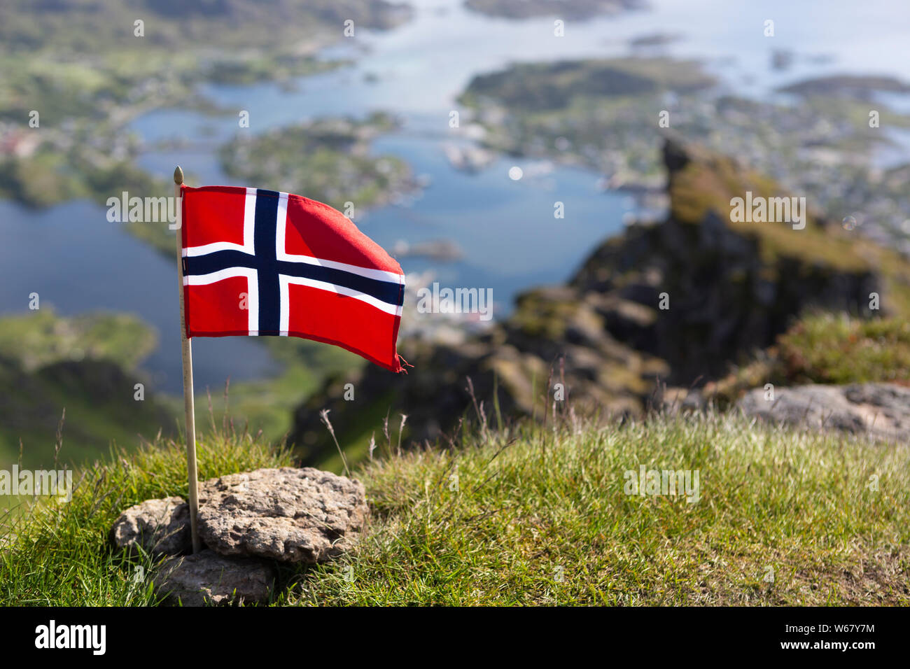 Bandiera norvegese sulla montagna Nonstinden. Sfocati sullo sfondo la visualizza in basso a Ballstad, Vestvågøya isola, isole Lofoten in Norvegia Foto Stock