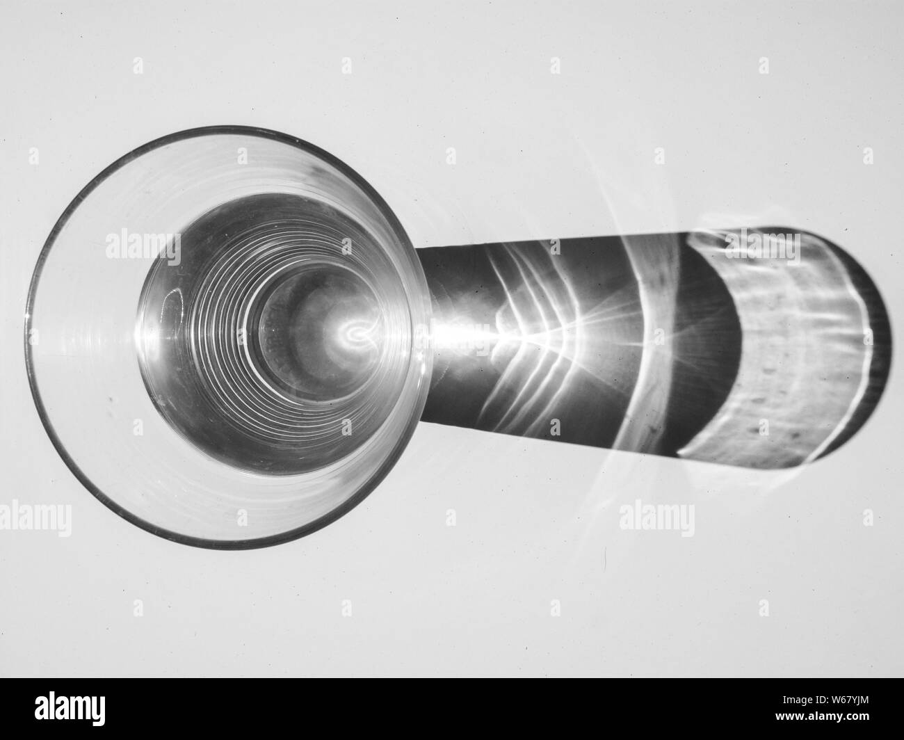 Foto di un bicchiere con acqua e ombra su una superficie bianca in bianco e nero Foto Stock