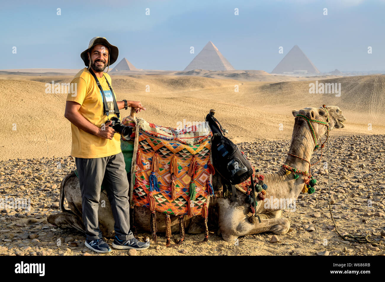 Mohamed e il suo cammello prendendo una pausa nel deserto con le piramidi di Giza in background Foto Stock