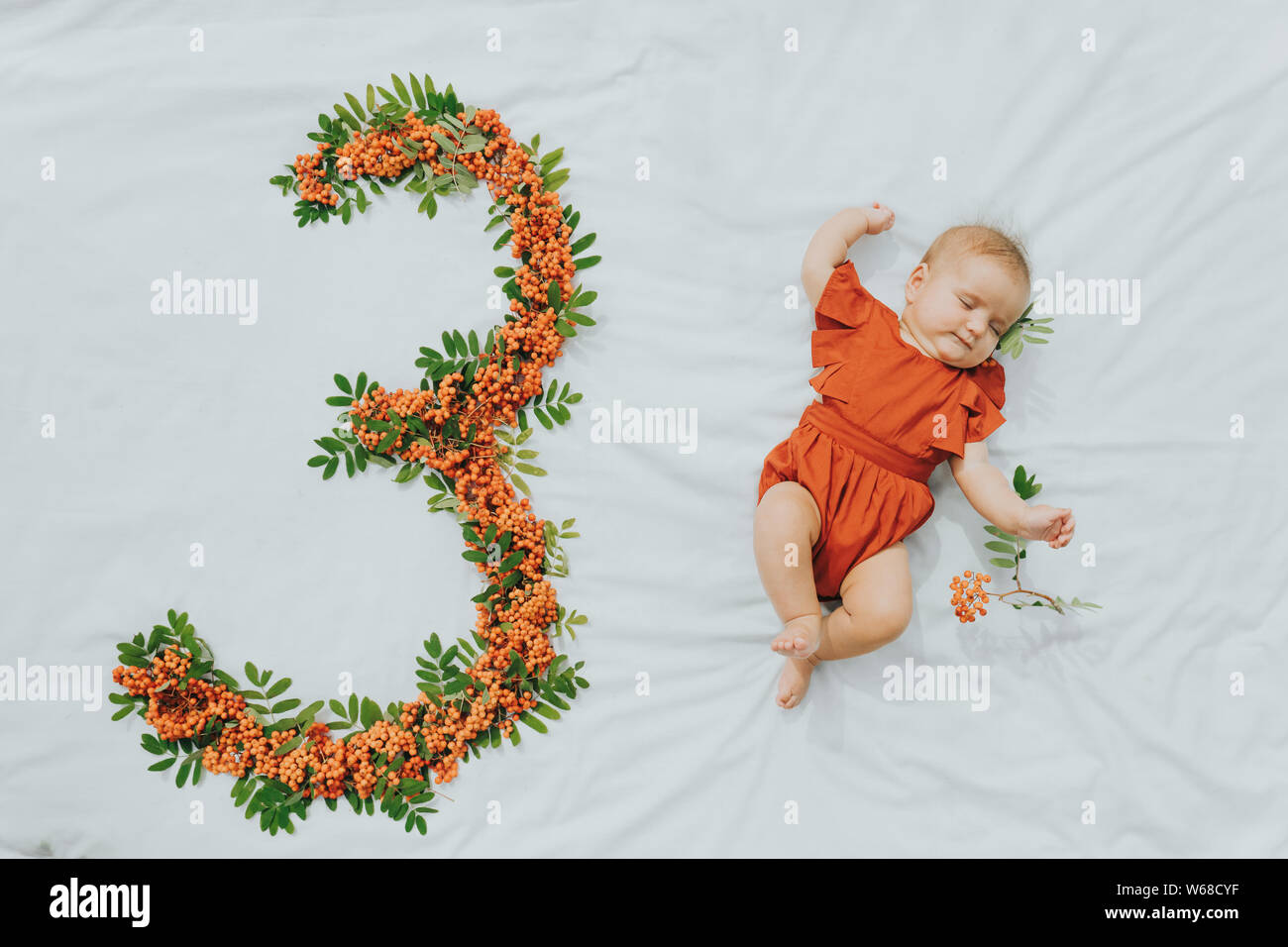 Tre mesi il bambino sdraiato sul foglio bianco accanto al fatto a mano numero fuori di rowan bacche e foglie Foto Stock