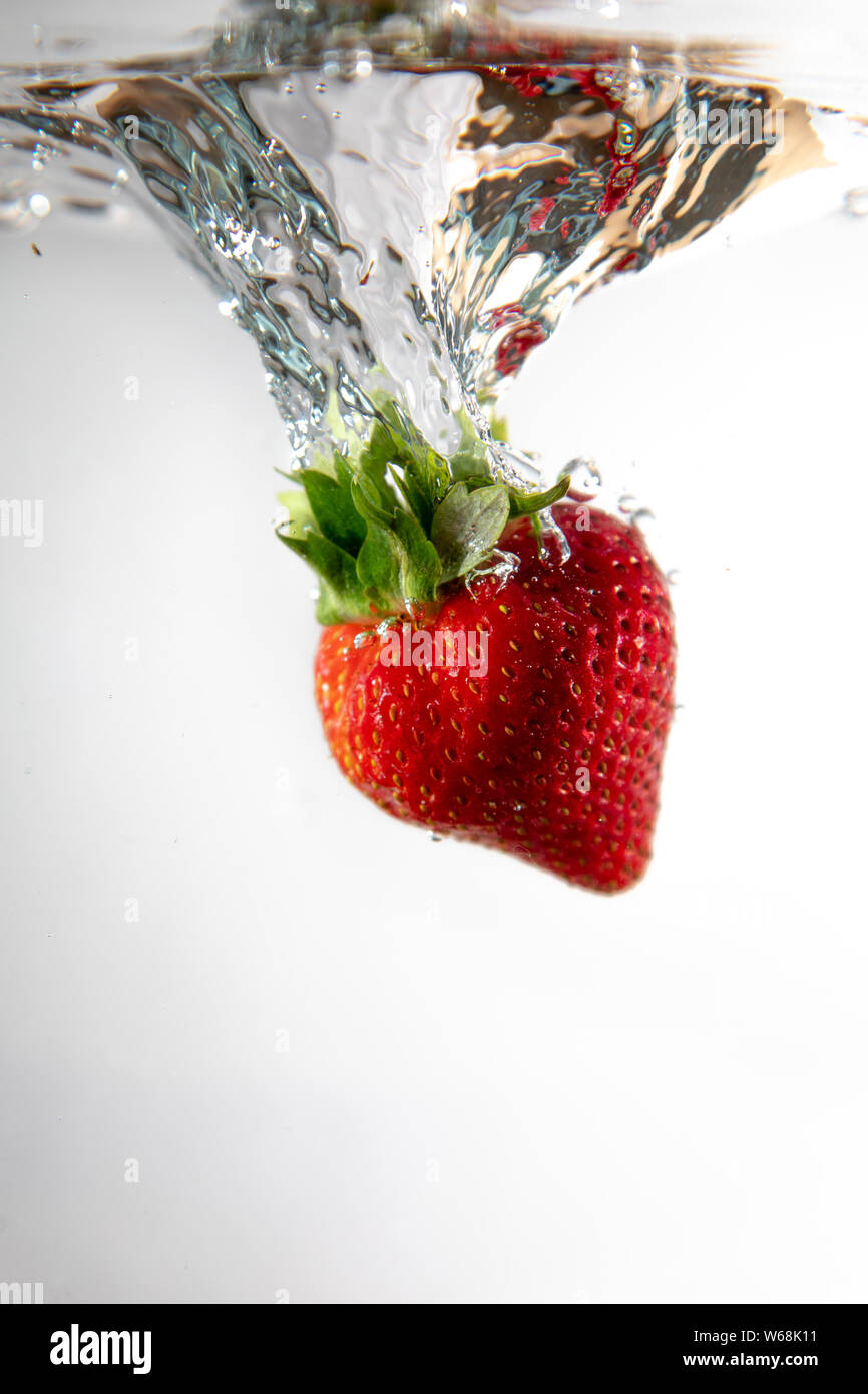 Un singolo strawberry cade in acqua creando una bella bolla di aria come fa. L'acqua si siede su uno sfondo bianco. Foto Stock