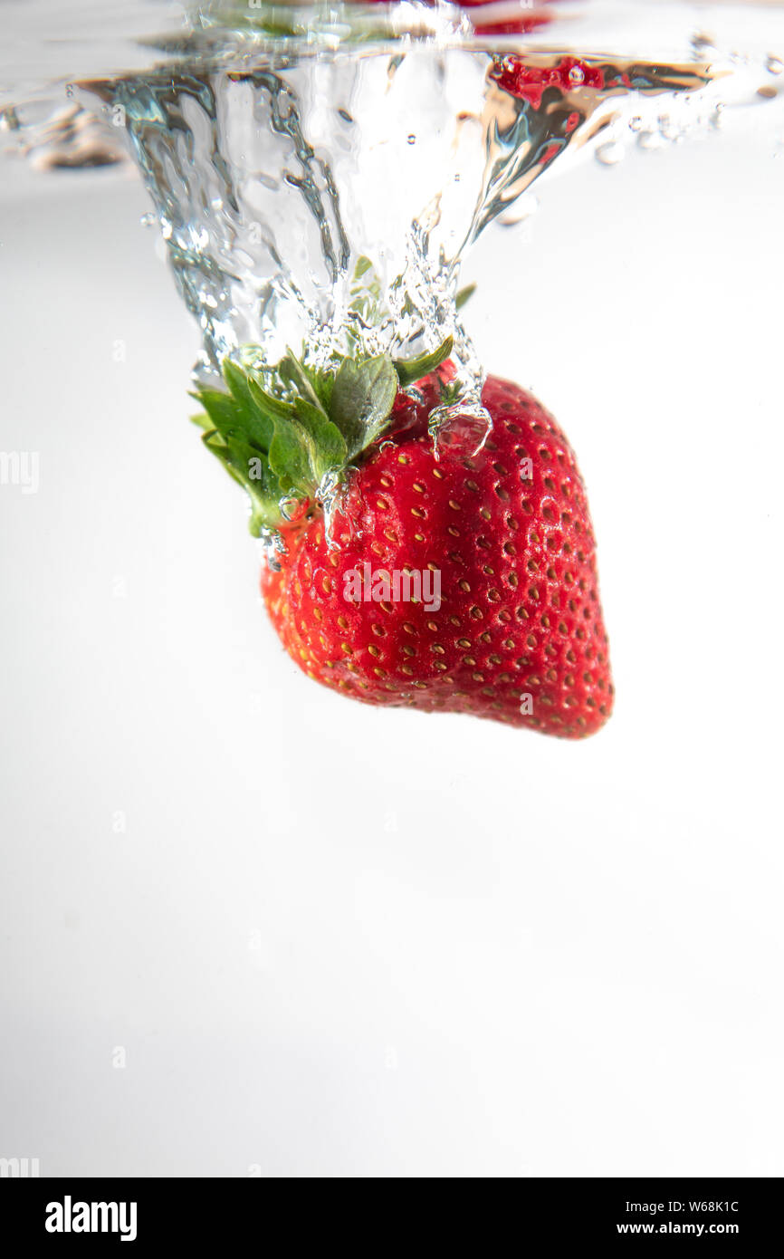 Un singolo strawberry cade in acqua creando una bella bolla di aria come fa. L'acqua si siede su uno sfondo bianco. Foto Stock