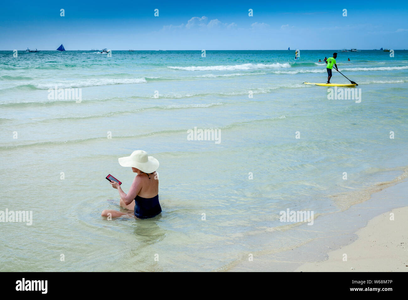 Una donna seduta in mare la lettura da un Kindle, White Beach, Boracay, Aklan, Filippine Foto Stock
