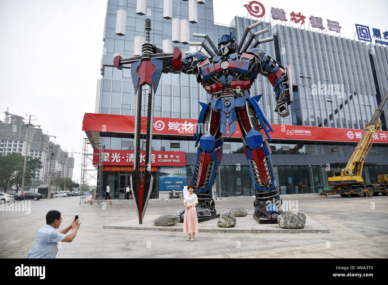 Locali residenti cinesi di scattare foto prima di una replica di Optimus Prime fatta di scarti di automobile di fronte a un complesso commerciale in Liaocheng ci Foto Stock