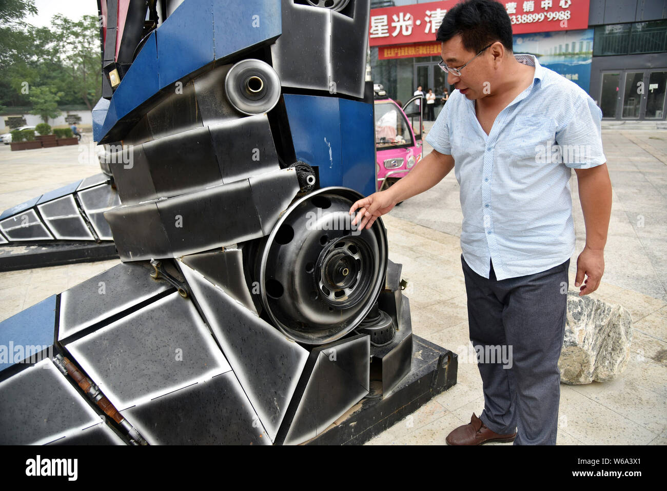 Un uomo cinese guarda a una replica di Optimus Prime fatta di scarti di automobile di fronte a un complesso commerciale in Liaocheng city, est della Cina di Shand Foto Stock