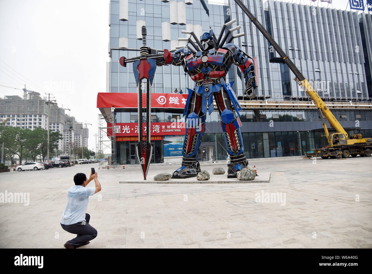 Un uomo cinese prende le immagini di una replica di Optimus Prime fatta di scarti di automobile di fronte a un complesso commerciale in Liaocheng city east mento Foto Stock