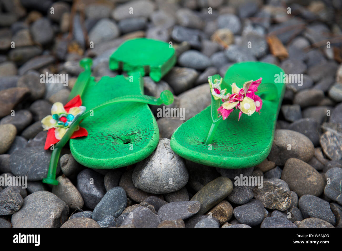 Ben amato jandals hanno finalmente rotto al punto da non poter essere indossato. Immagine mostra custom made jandals verde nel contesto su grigio pietre di fiume. Foto Stock