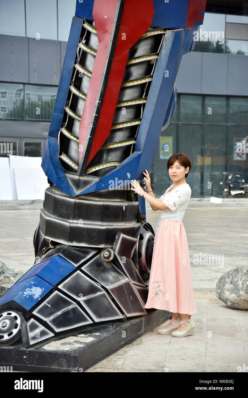 Una donna cinese pone per le foto con una replica di Optimus Prime fatta di scarti di automobile di fronte a un complesso commerciale in Liaocheng city, EAS Foto Stock