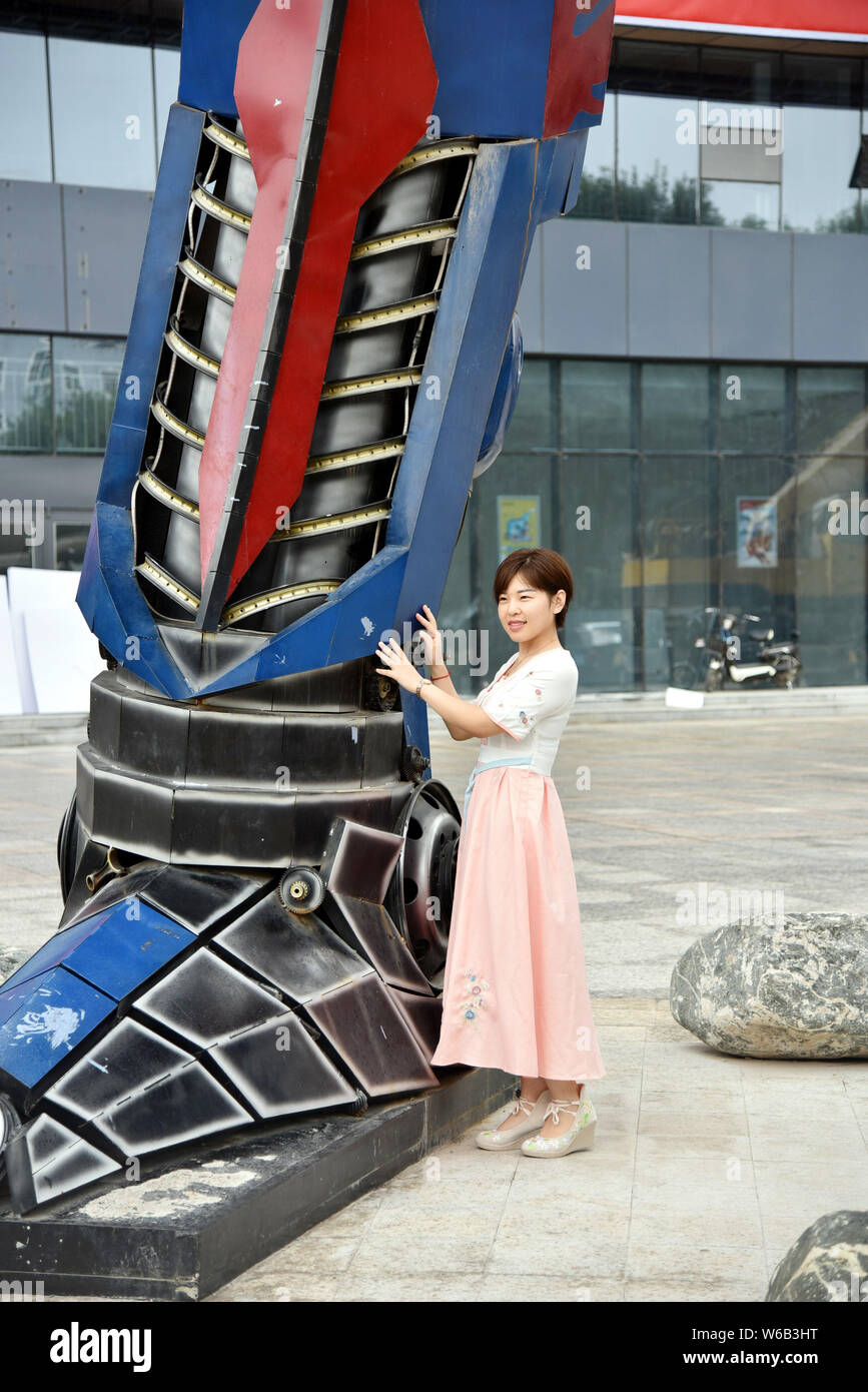 Una donna cinese pone per le foto con una replica di Optimus Prime fatta di scarti di automobile di fronte a un complesso commerciale in Liaocheng city, EAS Foto Stock