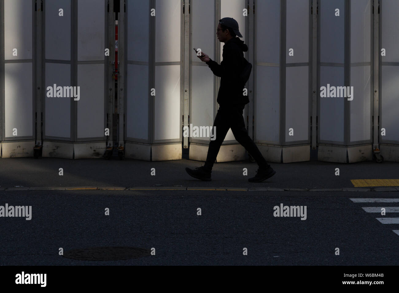 Un uomo giapponese che usa il suo smartphone mentre cammina davanti ad un ingresso di cantiere nelle strade di Shibuya, Tokyo, Giappone. Foto Stock