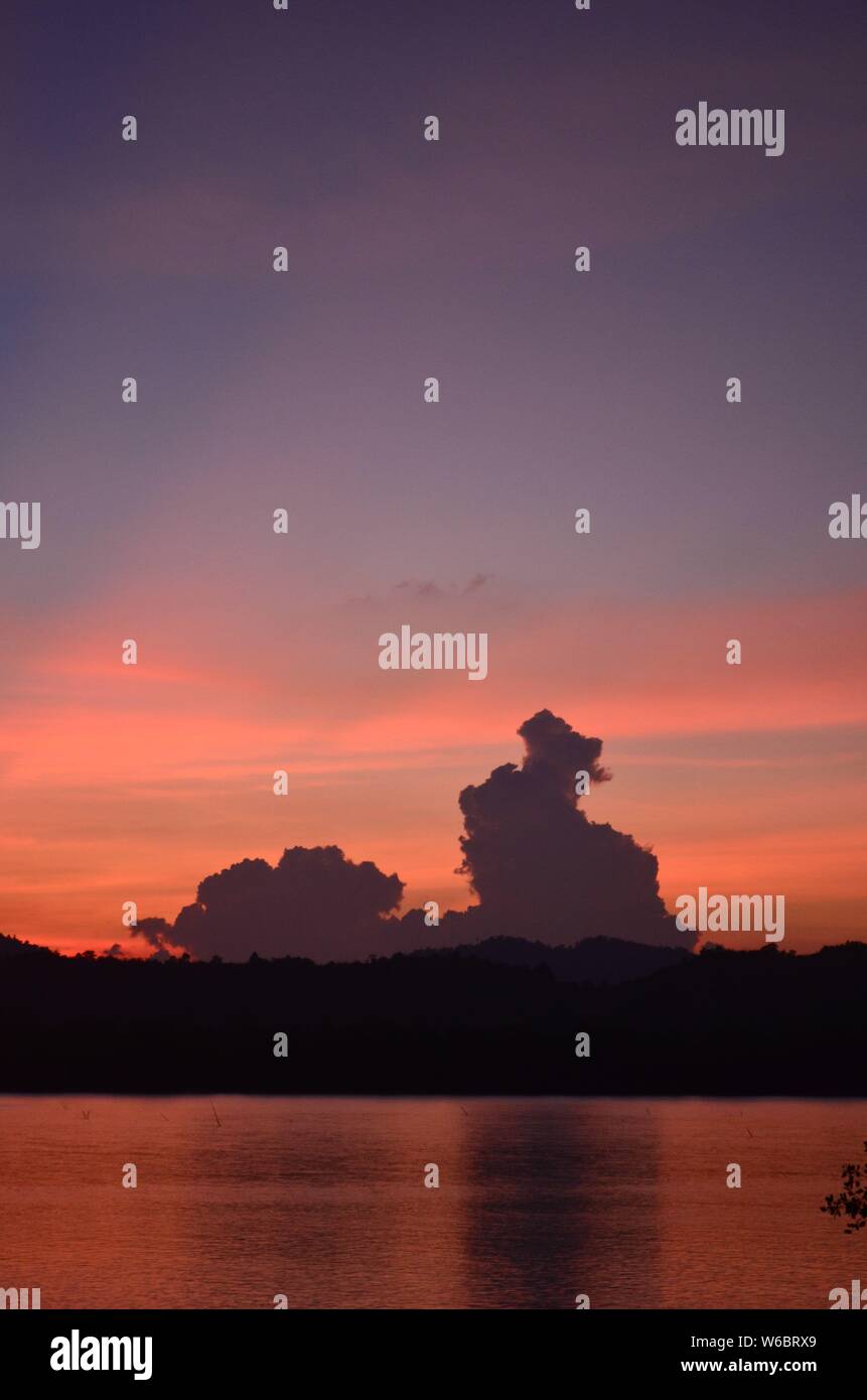 Il sole tramontare sull'Kra Buri fiume in Thailandia che si affaccia sul paesaggio di Myanmar. Le fronde delle palme fringe la parte superiore dell'immagine Foto Stock