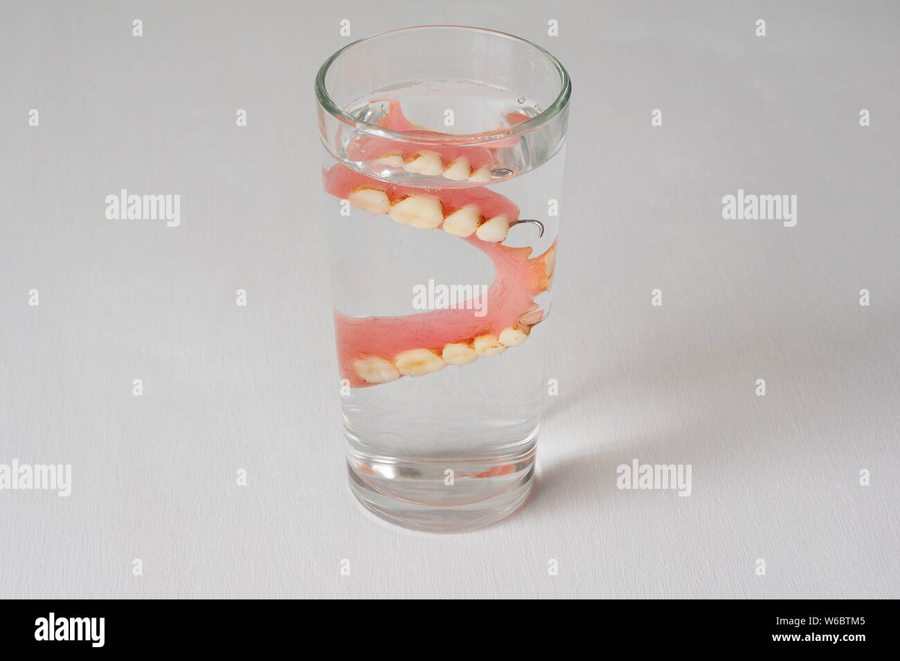 Dentiera in un bicchiere con acqua su uno sfondo bianco. Foto Stock