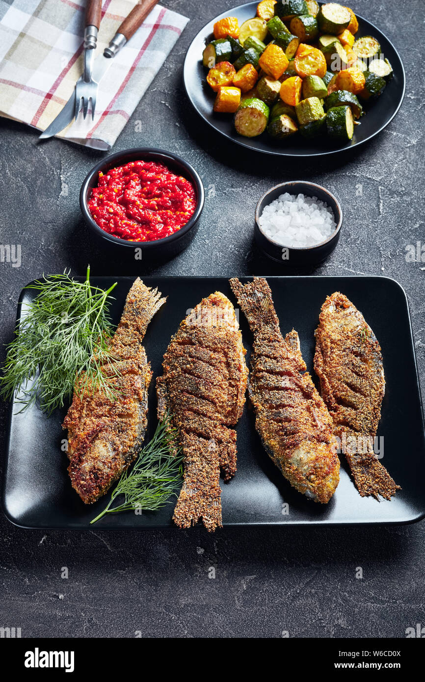 Fresco croccante fritti carassio carpe nero a piastra rettangolare su una tabella di calcestruzzo con zucchine fritte e salsa di pomodoro caldissima, verticale vista da sopra Foto Stock