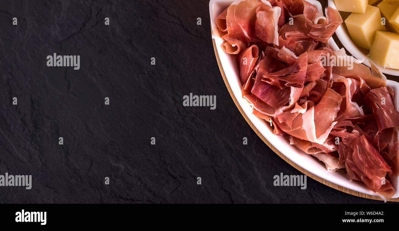 La birra snack e tapas: formaggio, prosciutto sulla piastra bianca su sfondo scuro. Alimenti e bevande Foto Stock