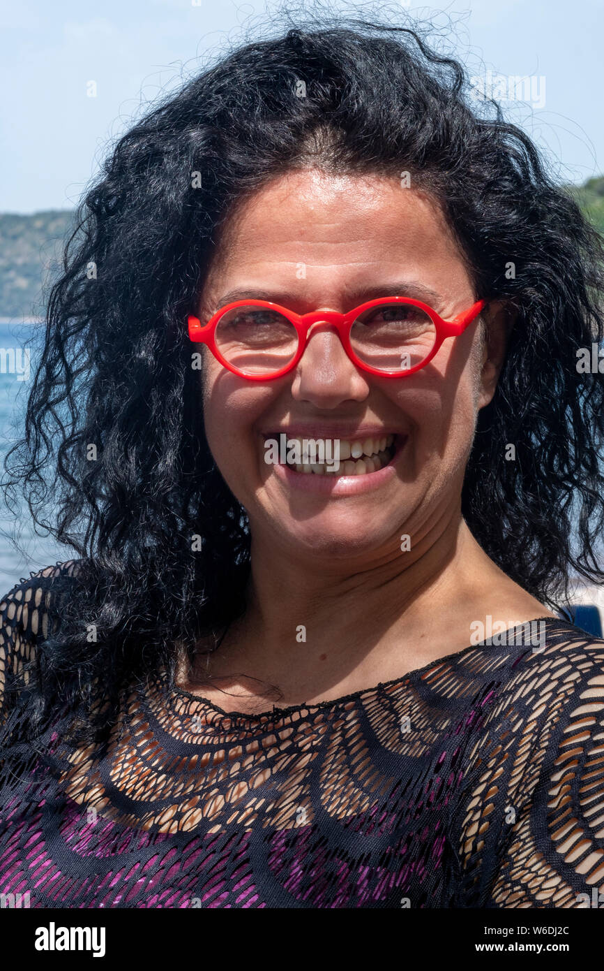 Donna attraente su una spiaggia in Grecia indossando rosso brillante occhiali da sole Foto Stock