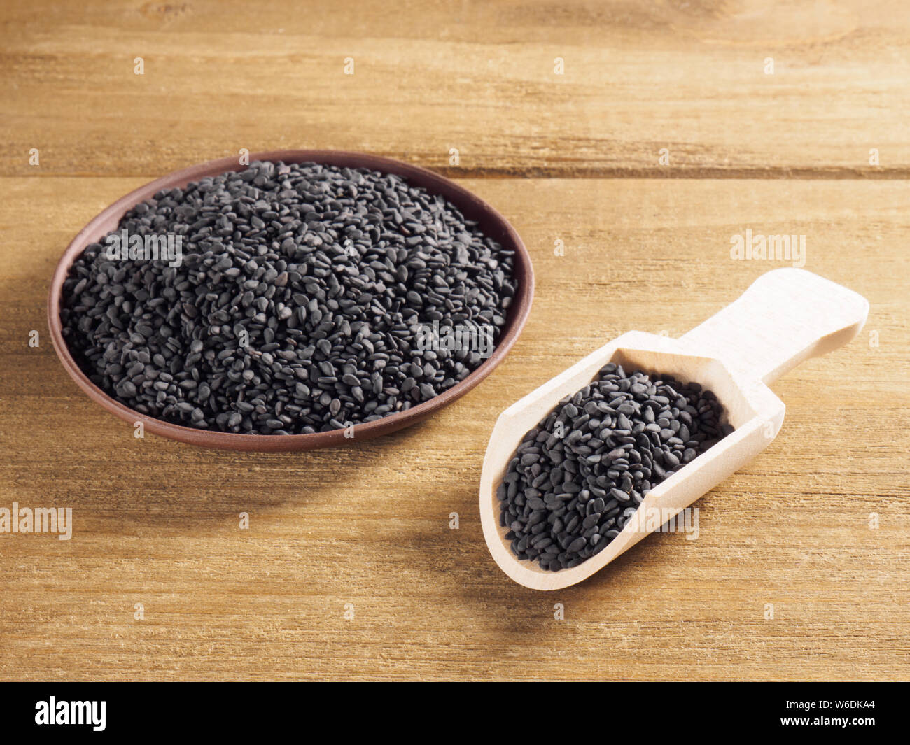 Il nero di sesamo (Sesamum indicum) in una piastra di argilla con il bianco scoop su uno sfondo di legno Foto Stock