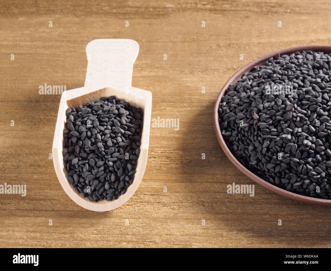 Il nero di sesamo (Sesamum indicum) in una piastra di argilla con il bianco scoop su uno sfondo di legno Foto Stock