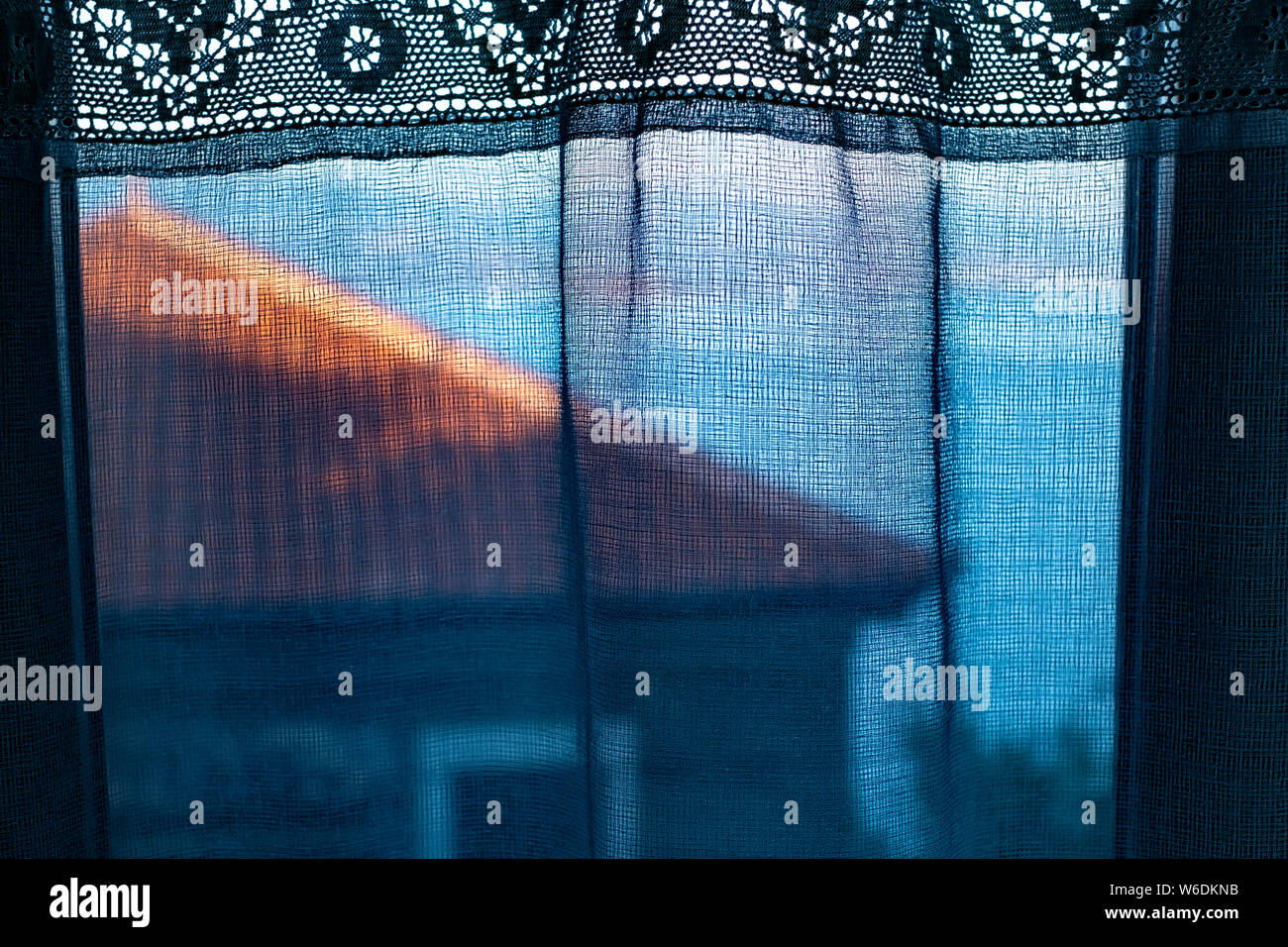 Vista del tetto di tegole di una vecchia casa greca e del Mar Egeo attraverso le tende di pizzo di un vicino di casa. Foto Stock