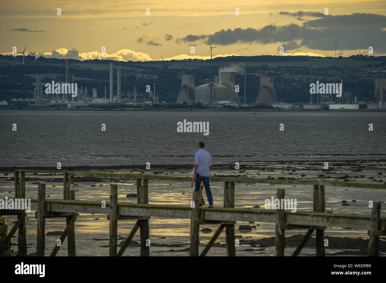 Padre e figlio a piedi sul molo con Ineos Grangemouth Petrolio e Gas raffineria in background. Foto Stock