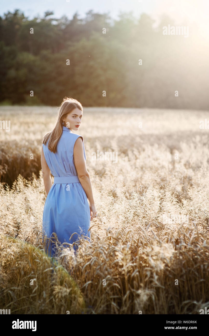 Vista posteriore di attraente donna bionda in vestito blu nel campo di grano. Dehors estivo concetto. Foto Stock